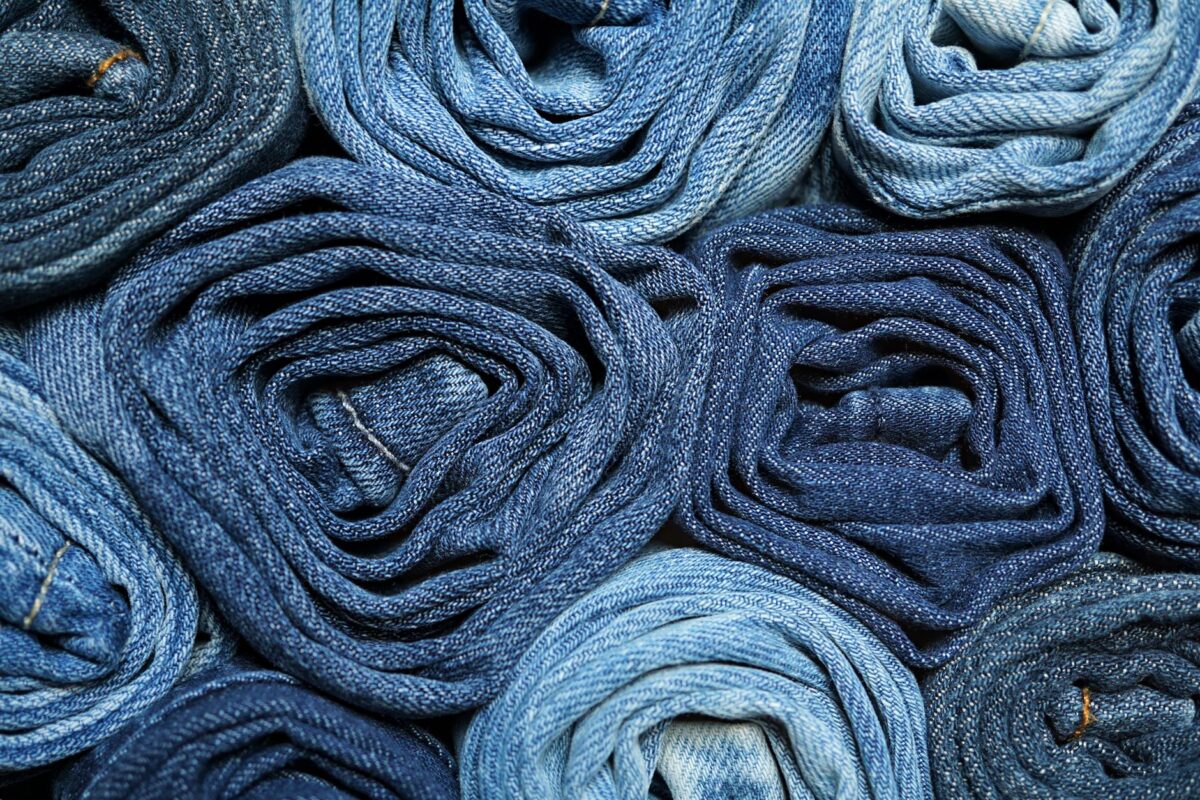 A close-up of rolled denim jeans arranged in a stack, showcasing shades of blue.